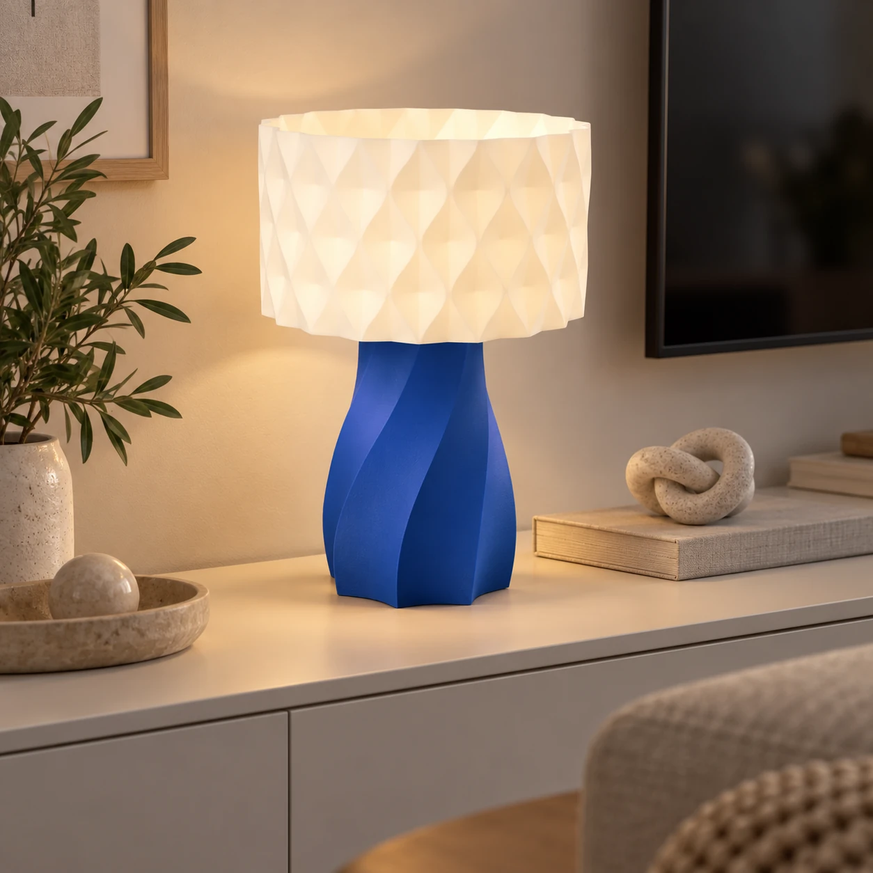 Pink Bnana Twirl Glow Table Lamp with royal blue base glowing beside books on a console